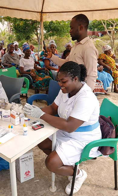 A dental assistant preparing supplies out side under a tent while patients wait behind her in chairs.